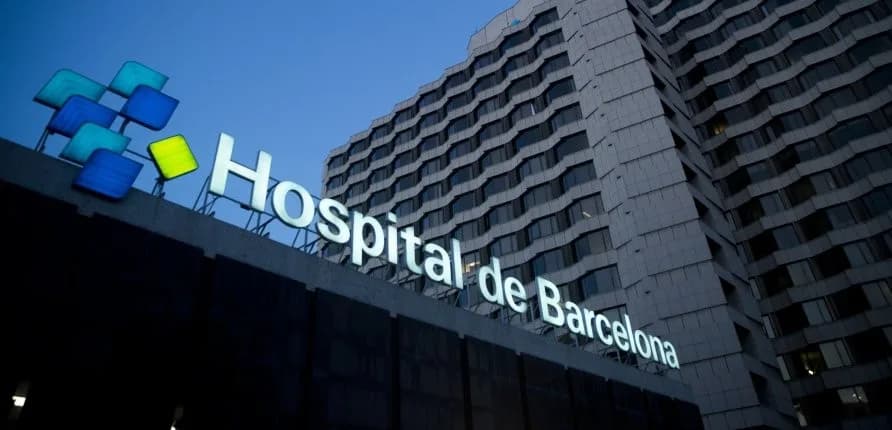 Fachada del Hospital de Barcelona al anochecer, con el rótulo iluminado sobre el edificio